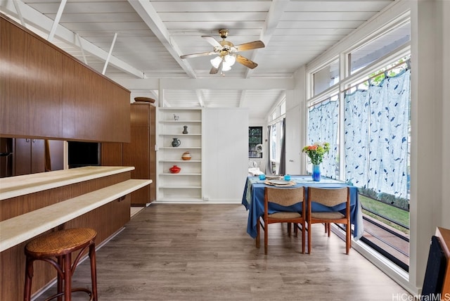 dining space with a ceiling fan, beam ceiling, and wood finished floors