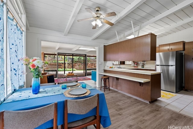 kitchen with light wood-style flooring, a breakfast bar area, freestanding refrigerator, vaulted ceiling with beams, and light countertops