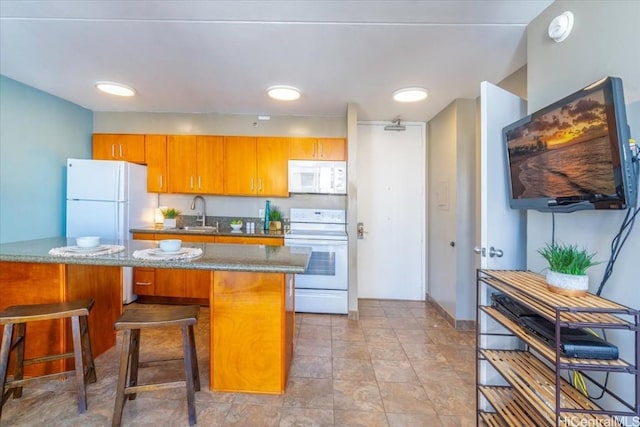 kitchen featuring white appliances, a sink, brown cabinets, dark stone countertops, and a kitchen bar