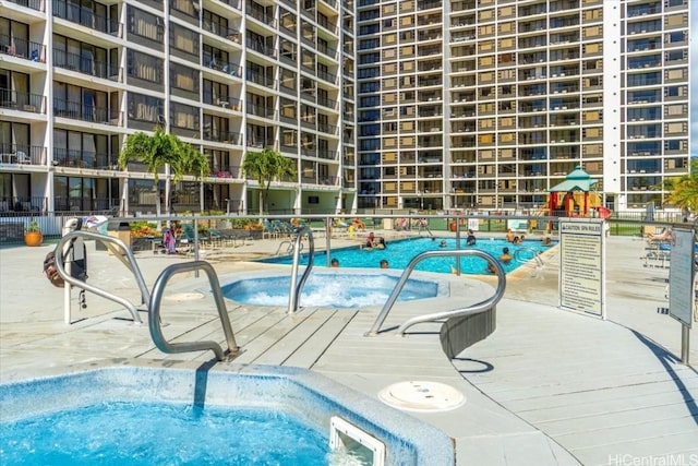 view of swimming pool with a community hot tub and fence