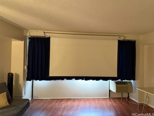 cinema featuring an AC wall unit, a textured ceiling, baseboards, and wood finished floors