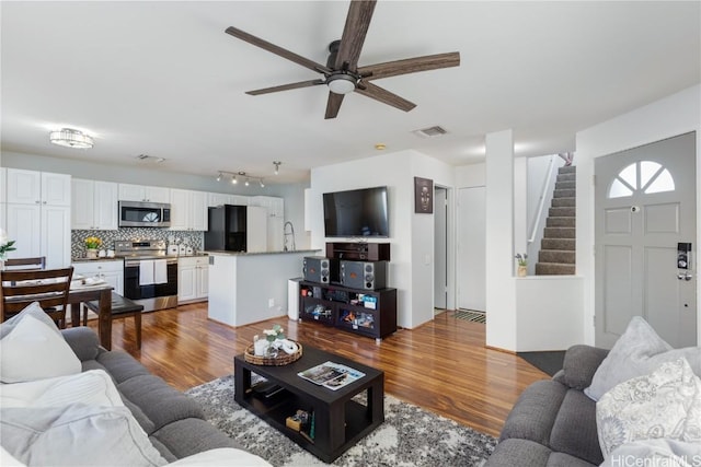 living area featuring a ceiling fan, visible vents, stairway, and wood finished floors