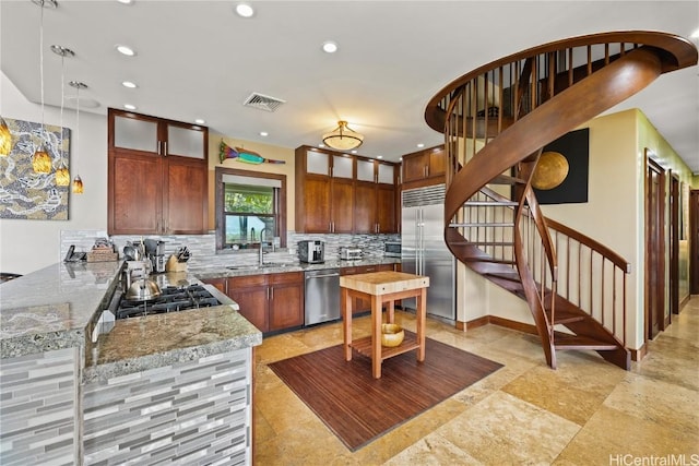 kitchen with visible vents, a sink, light stone countertops, stainless steel appliances, and backsplash