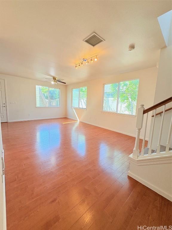 empty room with visible vents, stairway, wood-type flooring, baseboards, and ceiling fan