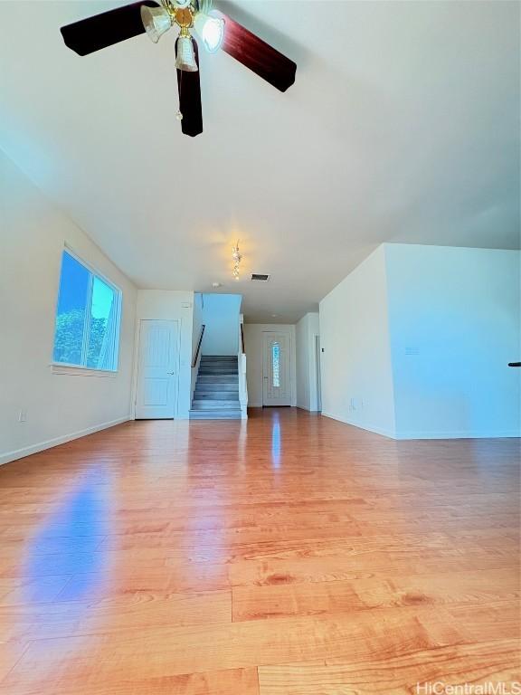 unfurnished living room featuring light wood-type flooring, stairway, baseboards, and a ceiling fan