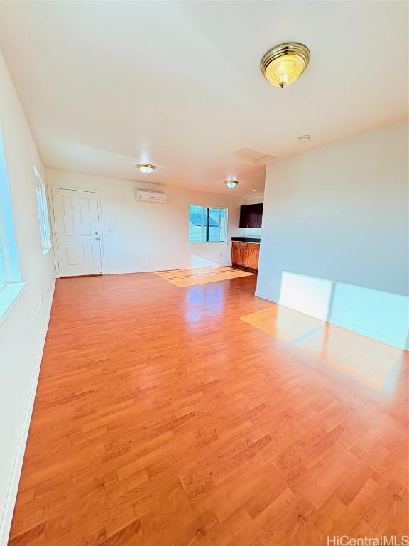 unfurnished room with a wall unit AC, baseboards, and light wood-type flooring