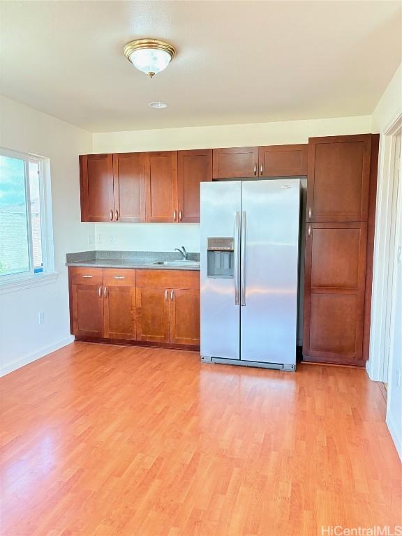 kitchen with baseboards, light wood finished floors, a sink, stainless steel refrigerator with ice dispenser, and brown cabinets