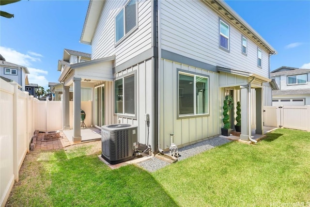 back of house featuring central AC unit, board and batten siding, a lawn, and a fenced backyard
