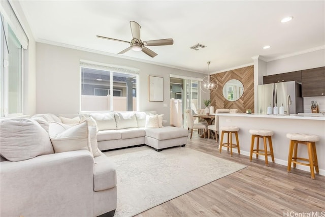 living room featuring visible vents, light wood-style flooring, crown molding, and ceiling fan with notable chandelier