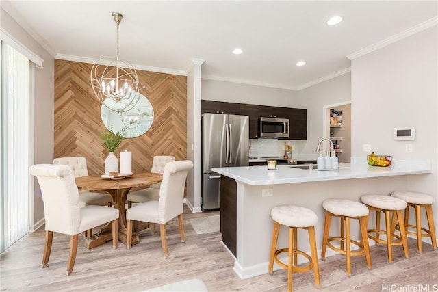 kitchen featuring a breakfast bar area, ornamental molding, stainless steel appliances, light countertops, and a chandelier