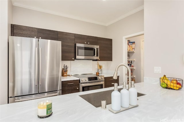 kitchen with a sink, appliances with stainless steel finishes, crown molding, light countertops, and dark brown cabinets