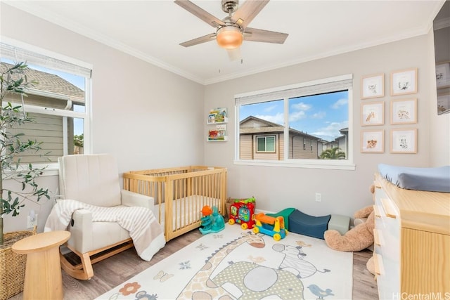 bedroom with multiple windows, a crib, wood finished floors, and ornamental molding