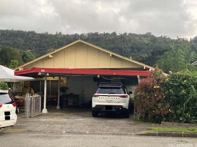 view of vehicle parking with driveway, a wooded view, and a detached carport