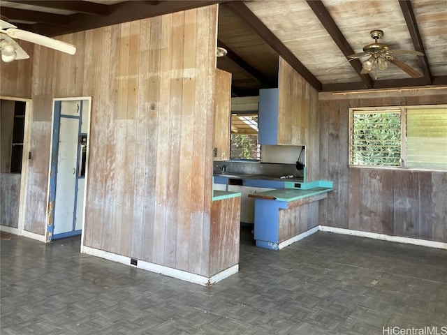 kitchen featuring vaulted ceiling with beams, wood walls, baseboards, and ceiling fan