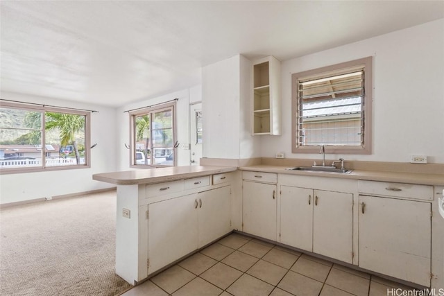 kitchen featuring a peninsula, a sink, light countertops, light carpet, and white cabinetry