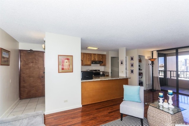 interior space with brown cabinets, light wood-style flooring, a textured ceiling, stainless steel range with electric stovetop, and under cabinet range hood