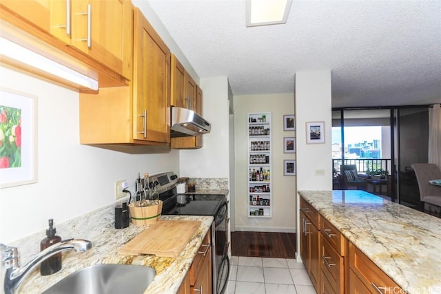 kitchen with a textured ceiling, under cabinet range hood, a sink, electric stove, and brown cabinetry