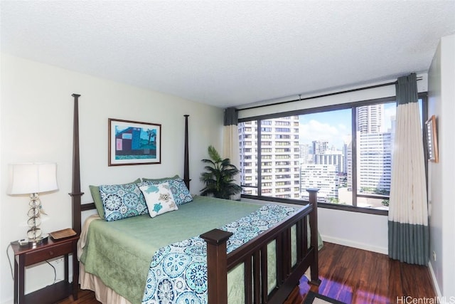 bedroom with a textured ceiling, baseboards, a city view, and wood finished floors