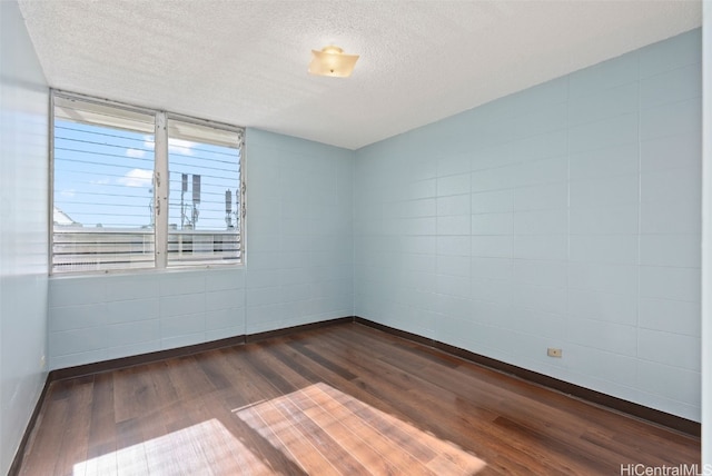 empty room featuring a textured ceiling, dark wood-style flooring, and baseboards