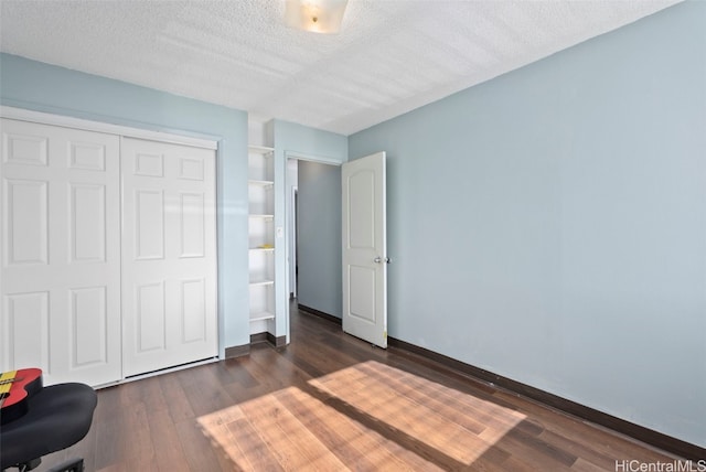 unfurnished bedroom with dark wood-style floors, a textured ceiling, a closet, and baseboards