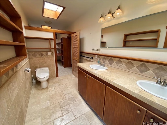 bathroom featuring double vanity, a skylight, a sink, stone tile flooring, and tile walls