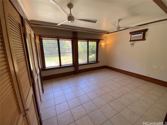 spare room with a wall unit AC, light tile patterned floors, baseboards, and a ceiling fan