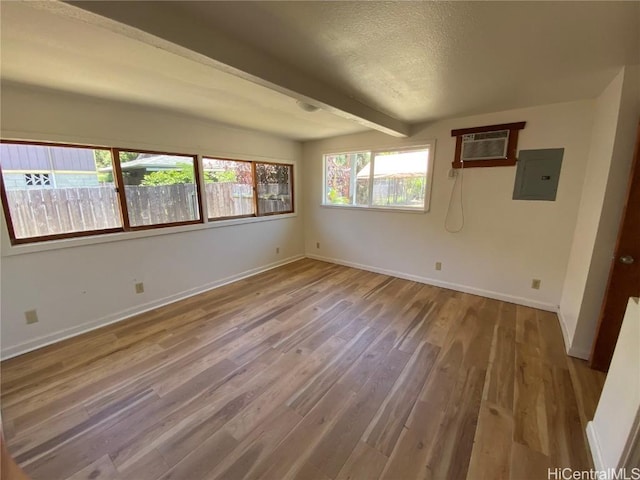 empty room featuring electric panel, beam ceiling, baseboards, and wood finished floors