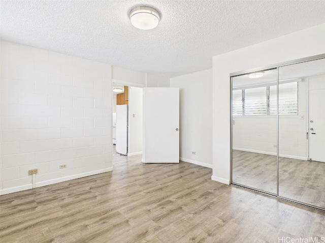 unfurnished bedroom with concrete block wall, wood finished floors, freestanding refrigerator, a closet, and a textured ceiling