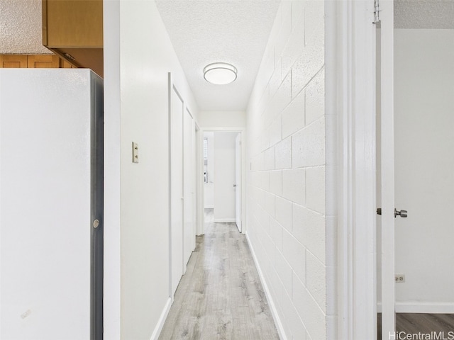 hallway featuring baseboards, a textured ceiling, concrete block wall, and light wood finished floors