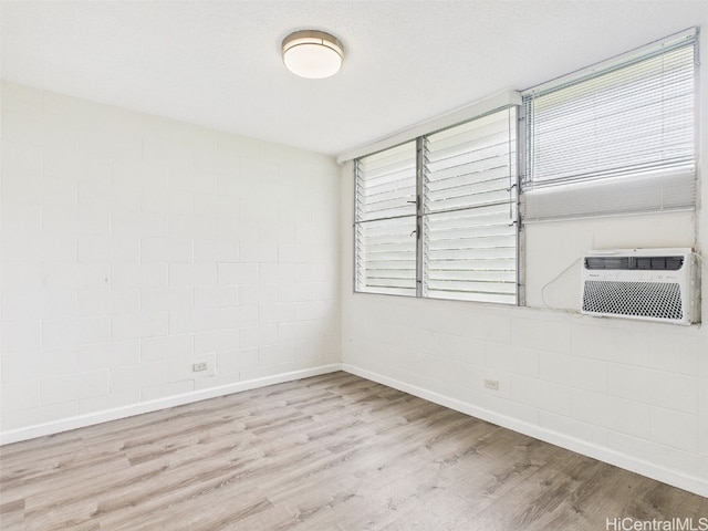 empty room with a healthy amount of sunlight, concrete block wall, baseboards, and wood finished floors