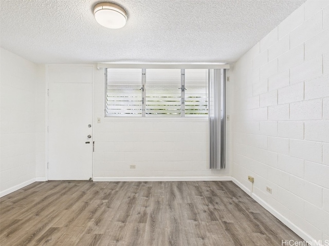 unfurnished room featuring baseboards, a textured ceiling, wood finished floors, and concrete block wall