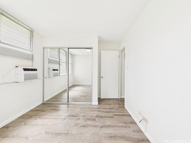 unfurnished bedroom featuring a closet, cooling unit, a textured ceiling, and wood finished floors