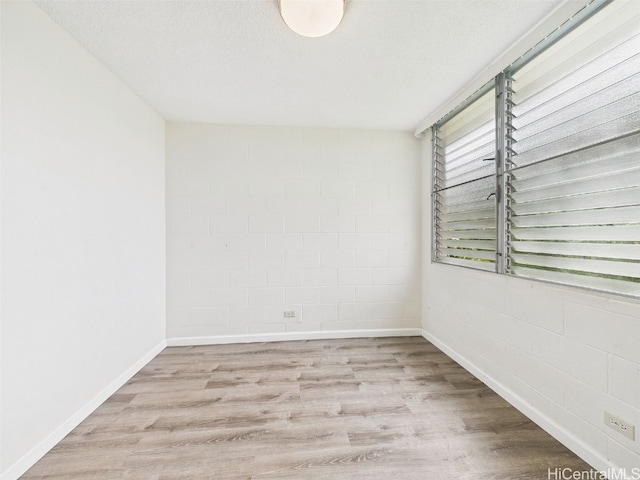 spare room featuring a textured ceiling, concrete block wall, baseboards, and wood finished floors