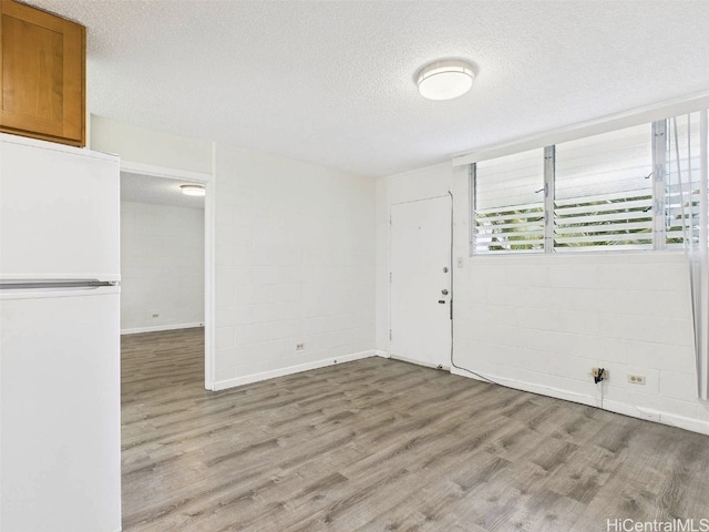 spare room with light wood-style flooring, concrete block wall, and a textured ceiling