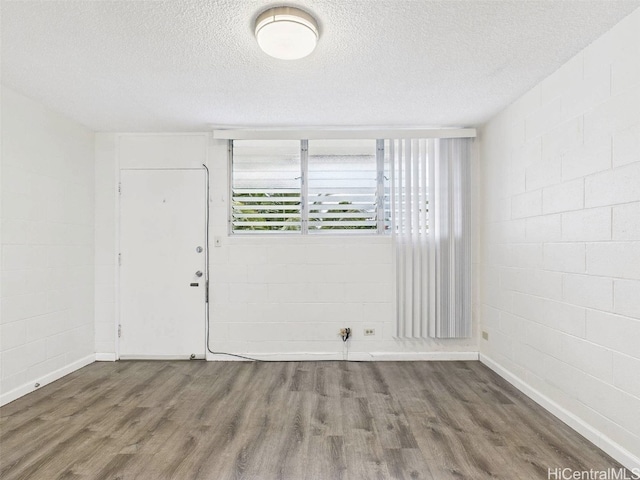 spare room with a textured ceiling, concrete block wall, and wood finished floors