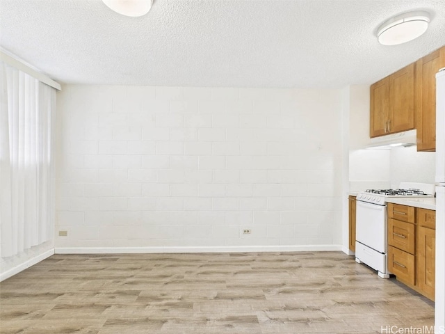 kitchen with under cabinet range hood, a textured ceiling, light wood-type flooring, and white range with gas stovetop