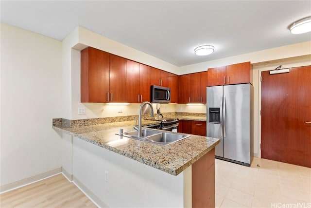 kitchen featuring a peninsula, a sink, baseboards, appliances with stainless steel finishes, and brown cabinetry