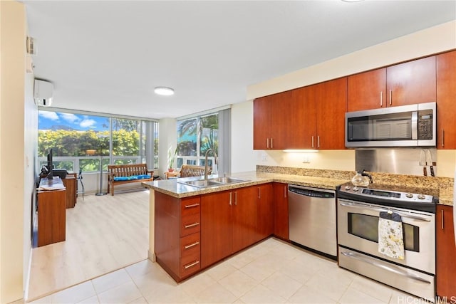 kitchen with a peninsula, a sink, an AC wall unit, appliances with stainless steel finishes, and light stone countertops