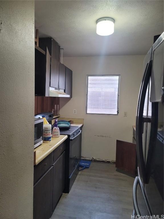 kitchen featuring light countertops, a textured ceiling, light wood-type flooring, under cabinet range hood, and black appliances