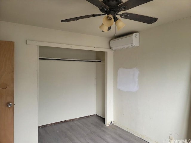 unfurnished bedroom featuring ceiling fan, wood finished floors, baseboards, an AC wall unit, and a closet