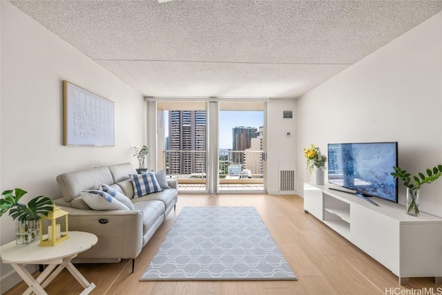 living area with a wall of windows, wood finished floors, visible vents, and a textured ceiling