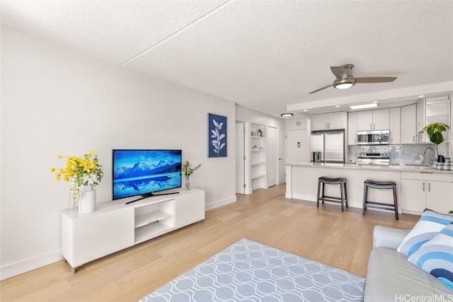 living room featuring a textured ceiling, baseboards, light wood-type flooring, and ceiling fan