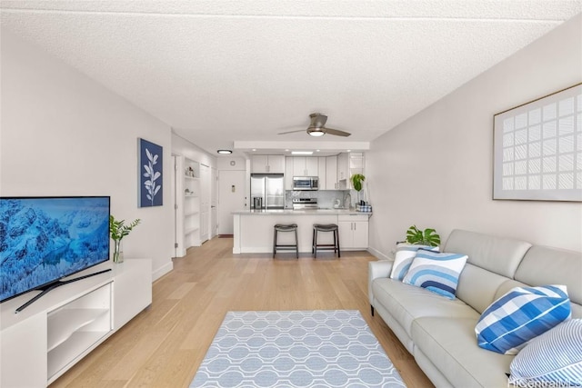 living room featuring baseboards, a textured ceiling, light wood-type flooring, and ceiling fan