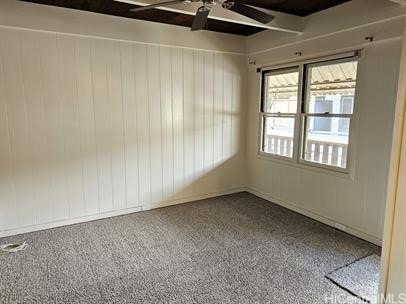 carpeted spare room featuring ceiling fan and wood walls