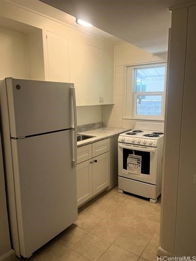 kitchen with white appliances, white cabinetry, light countertops, and light tile patterned flooring