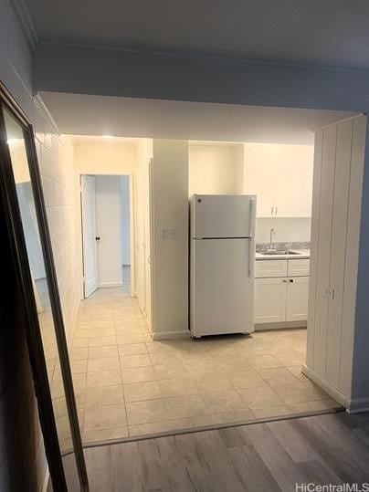 kitchen featuring light wood-type flooring, freestanding refrigerator, white cabinets, and a sink