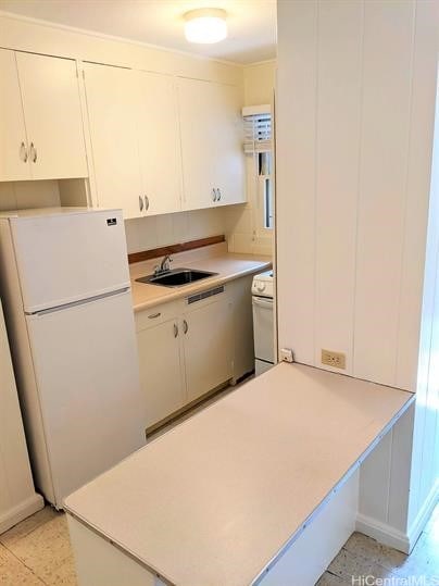 kitchen featuring white cabinets, stove, freestanding refrigerator, light countertops, and a sink