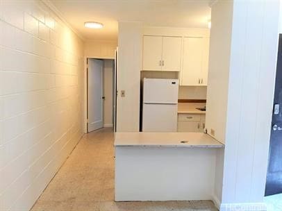 kitchen with a peninsula, white cabinetry, light countertops, freestanding refrigerator, and concrete block wall