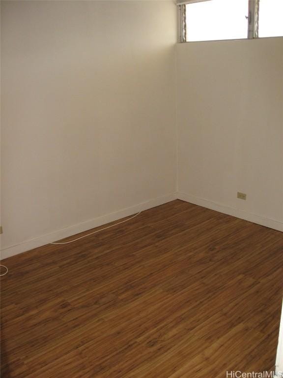 spare room featuring dark wood-style flooring and baseboards