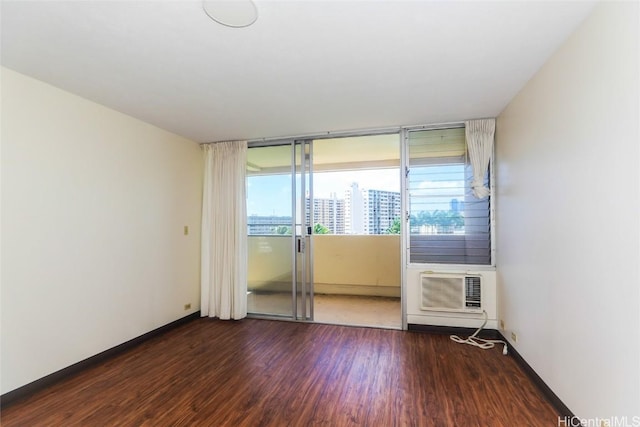 spare room with a city view, baseboards, an AC wall unit, and wood finished floors